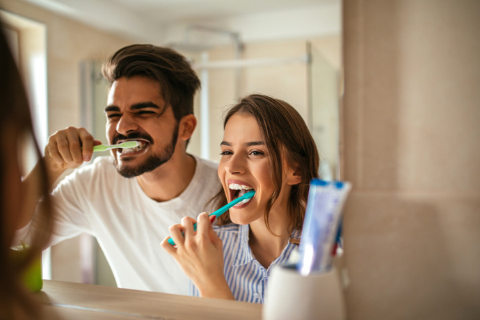 Pareja joven sonriendo frente al espejo mientras se lavan los dientes