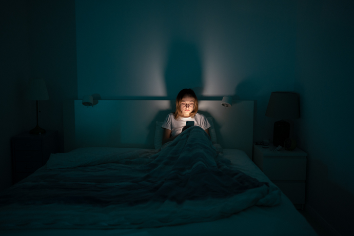 mujer en la cama a oscuras mirando su celular