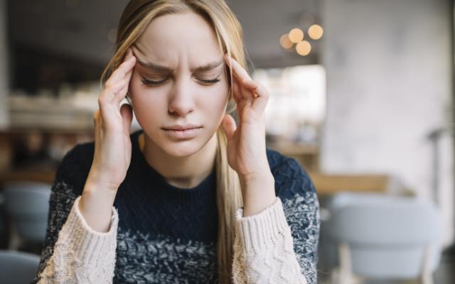 Mujer joven con migraña intensa sosteniendo su cabeza por el dolor.