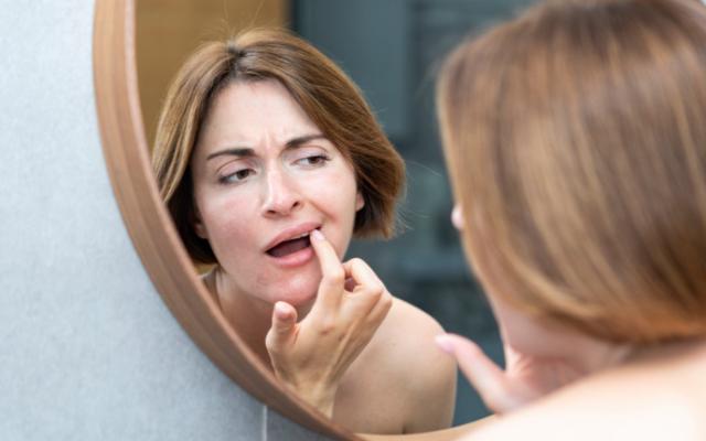 Mujer examinando en el espejo sus manchas marrones en los dientes. 