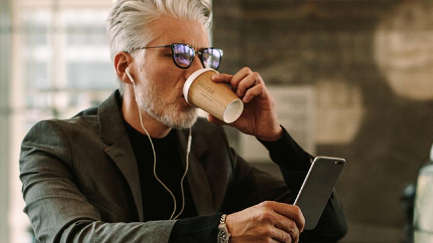 Hombre tomando café mientras observa su celular
