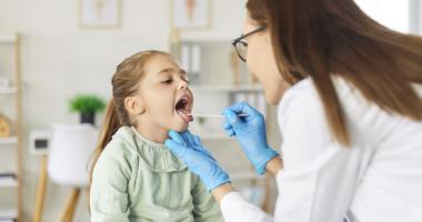Doctora examinando si niña tiene pus en la garganta.